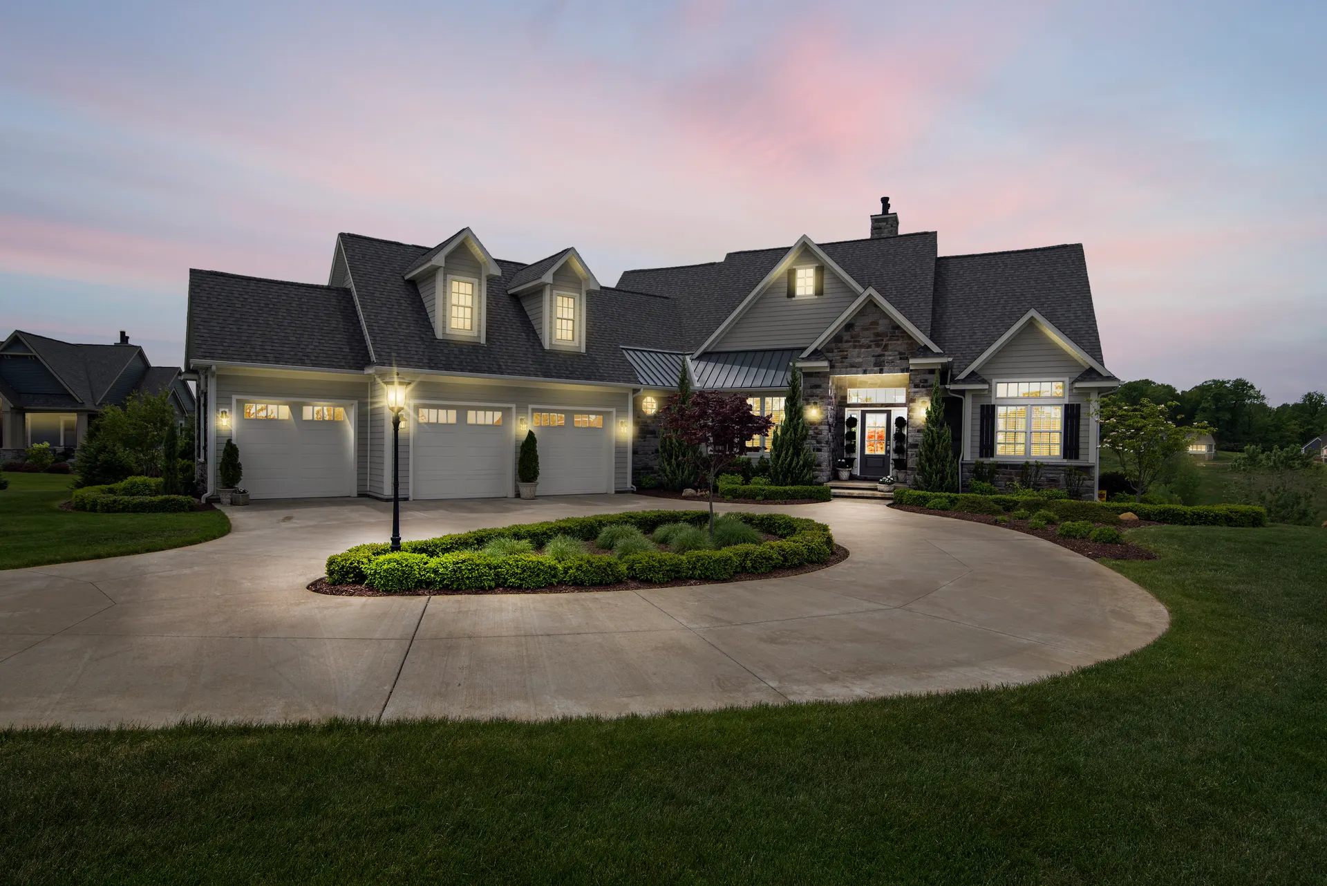 Modern New Jersey home at dusk with an illuminated two-car garage door and curved driveway
